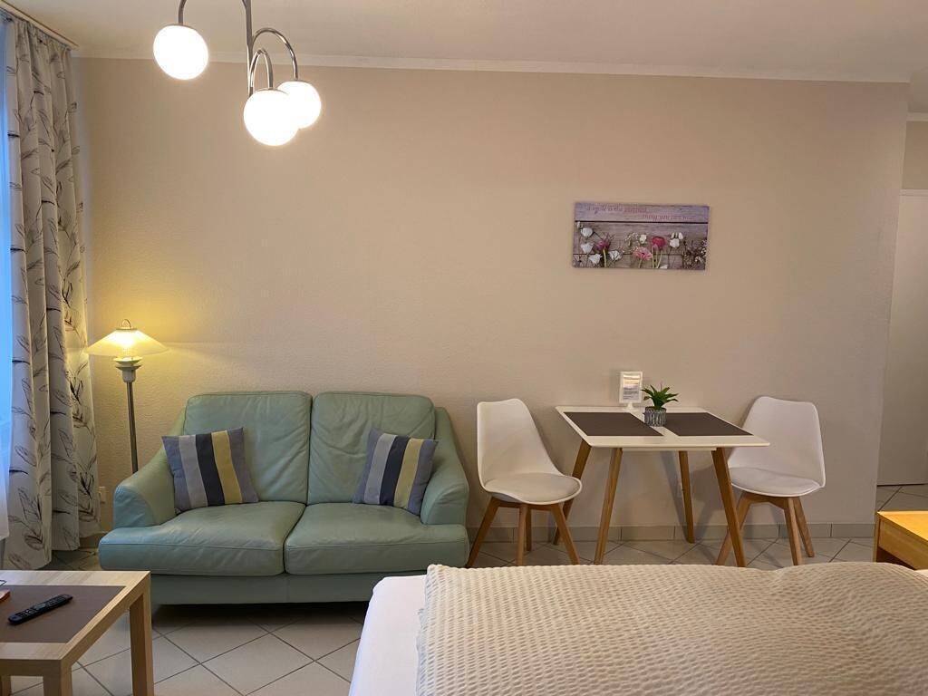 A cozy room with a green sofa, a small table, a bed, and a dining area with two chairs.