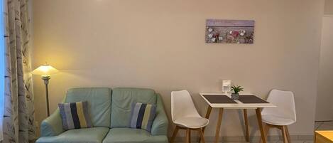 A cozy room with a green sofa, a small table, a bed, and a dining area with two chairs.