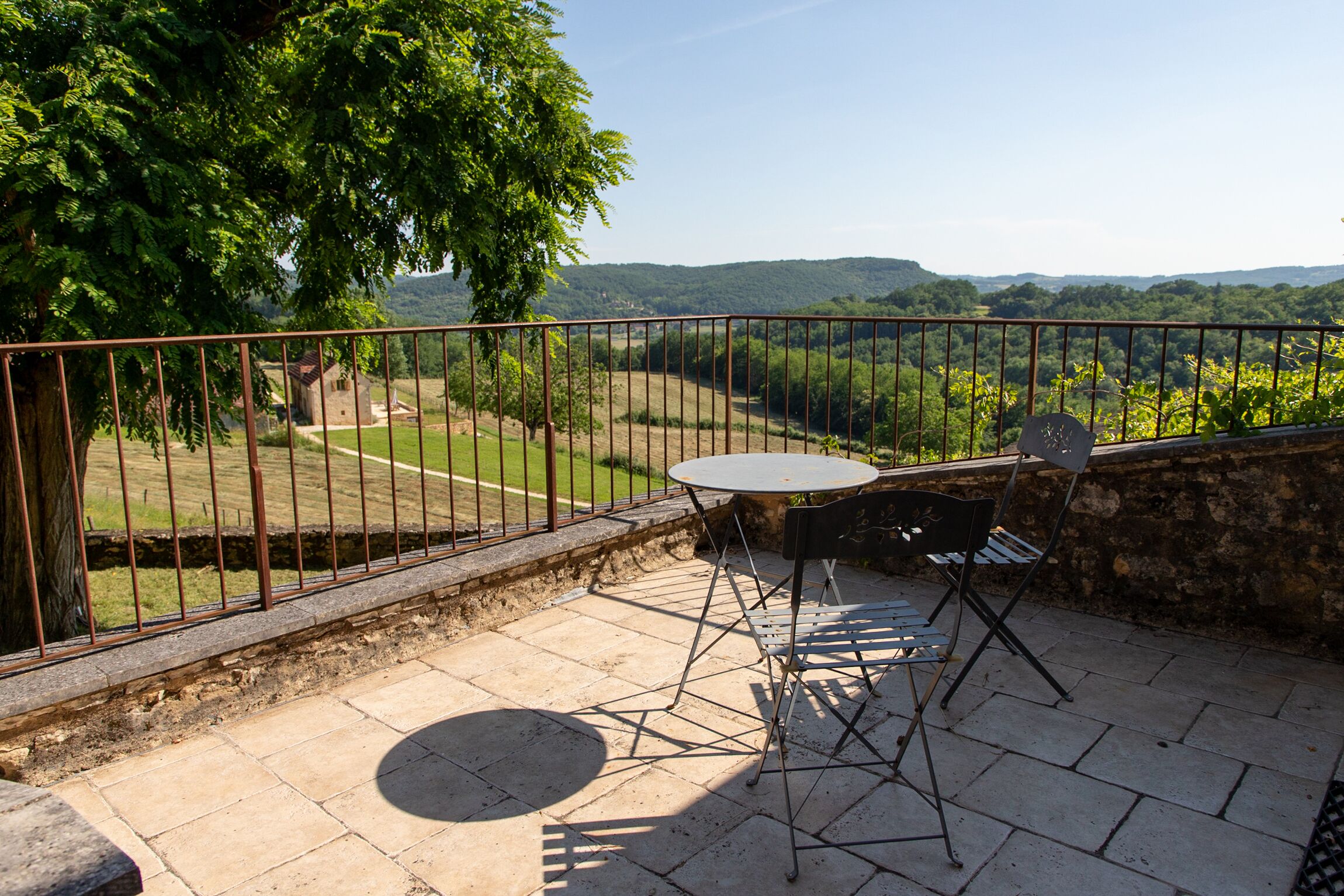 Un patio exterior con una mesa y sillas, con vistas a un paisaje pintoresco con colinas y una zona vallada.