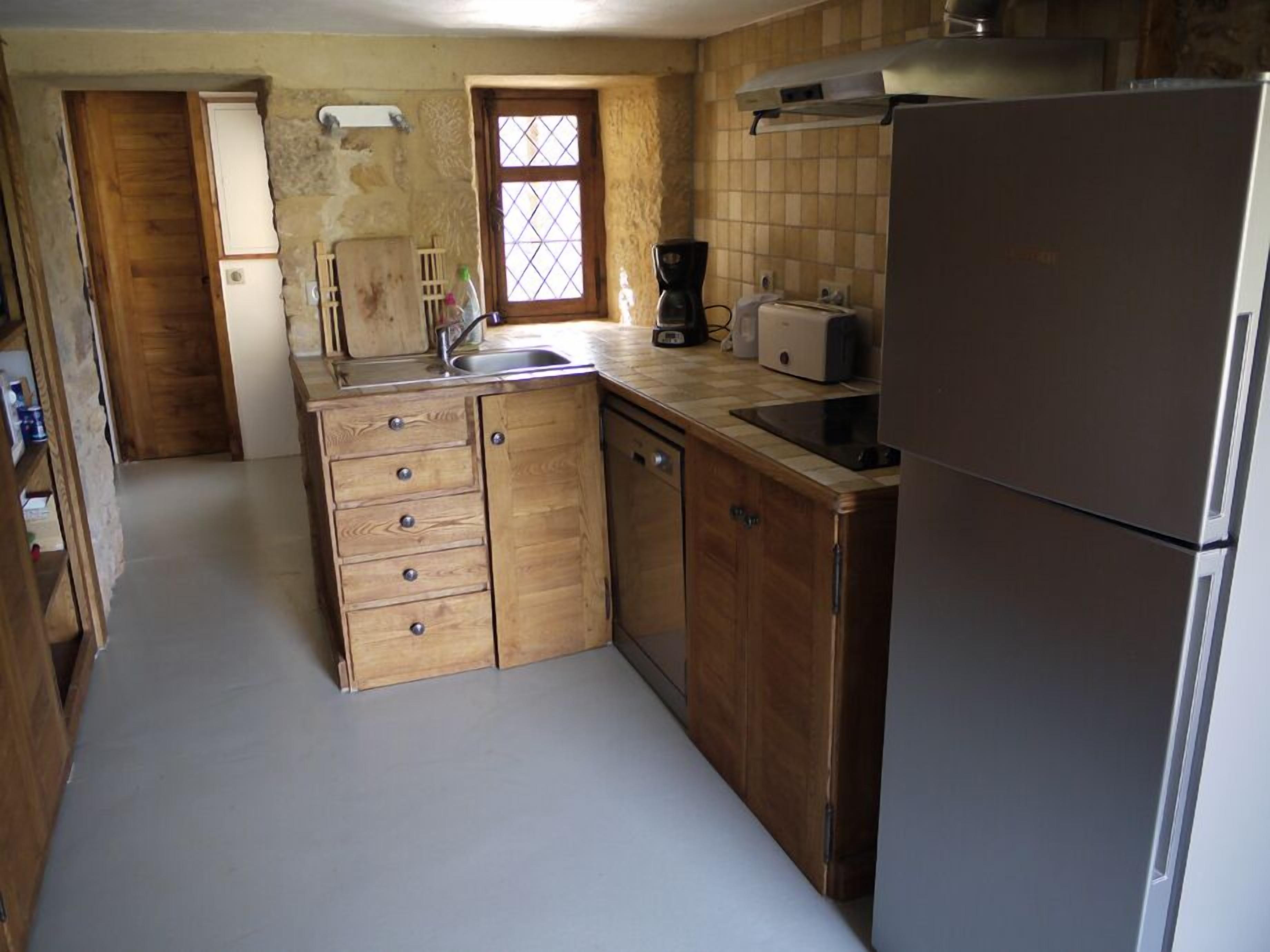 Una cucina compatta con mobili in legno, lavello integrato, tostapane e frigorifero.