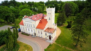 A large, historic building with a red-tiled roof, a central tower, and a formal entrance.