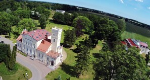 An aerial view of a large building with a prominent tower, surrounded by lush greenery and a well-maintained lawn.