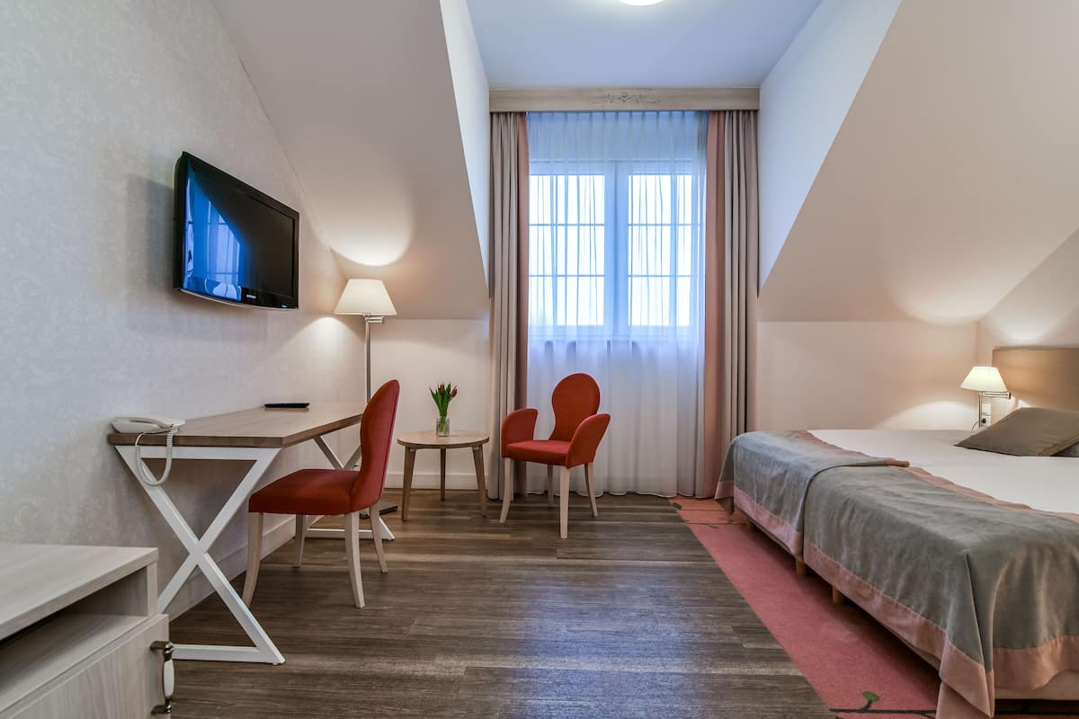 Une chambre d’hôtel équipée d’un bureau, de deux chaises, d’un lit, d’un téléviseur fixé au mur et d’une fenêtre avec des rideaux.
