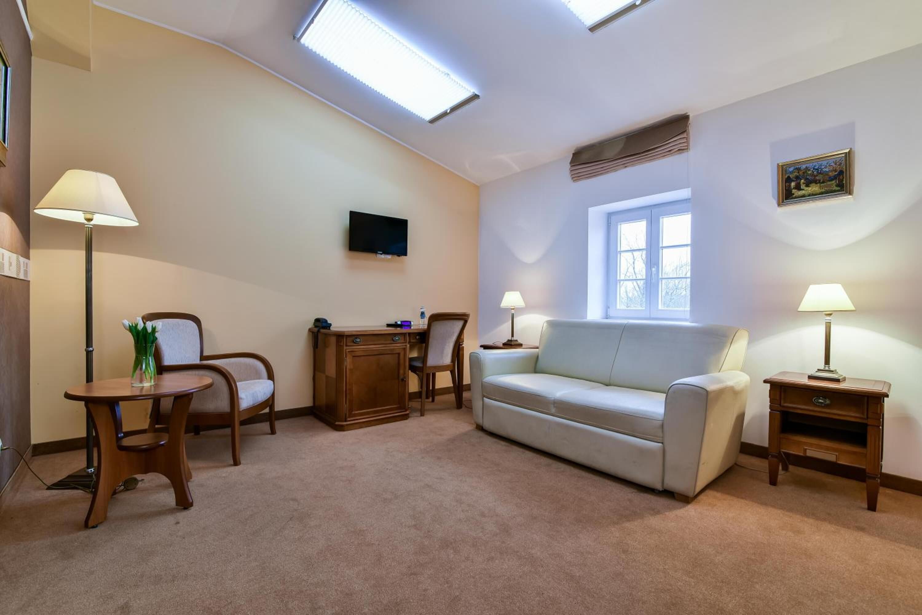 A living room with a sofa, two chairs, a small table, a TV, and a window.