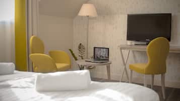 Habitación de hotel con una cama, dos sillones amarillos, un escritorio con una computadora portátil, un televisor y una lámpara de pie.