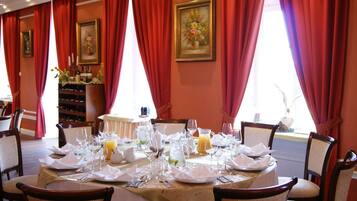 A dining area with a table set for four, red curtains, and a wine rack in the background.