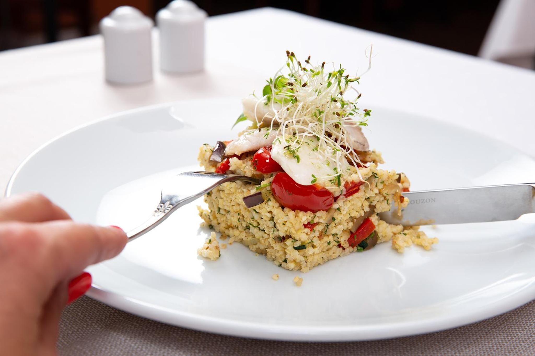 A white plate with a food dish topped with sprouts and cherry tomatoes.