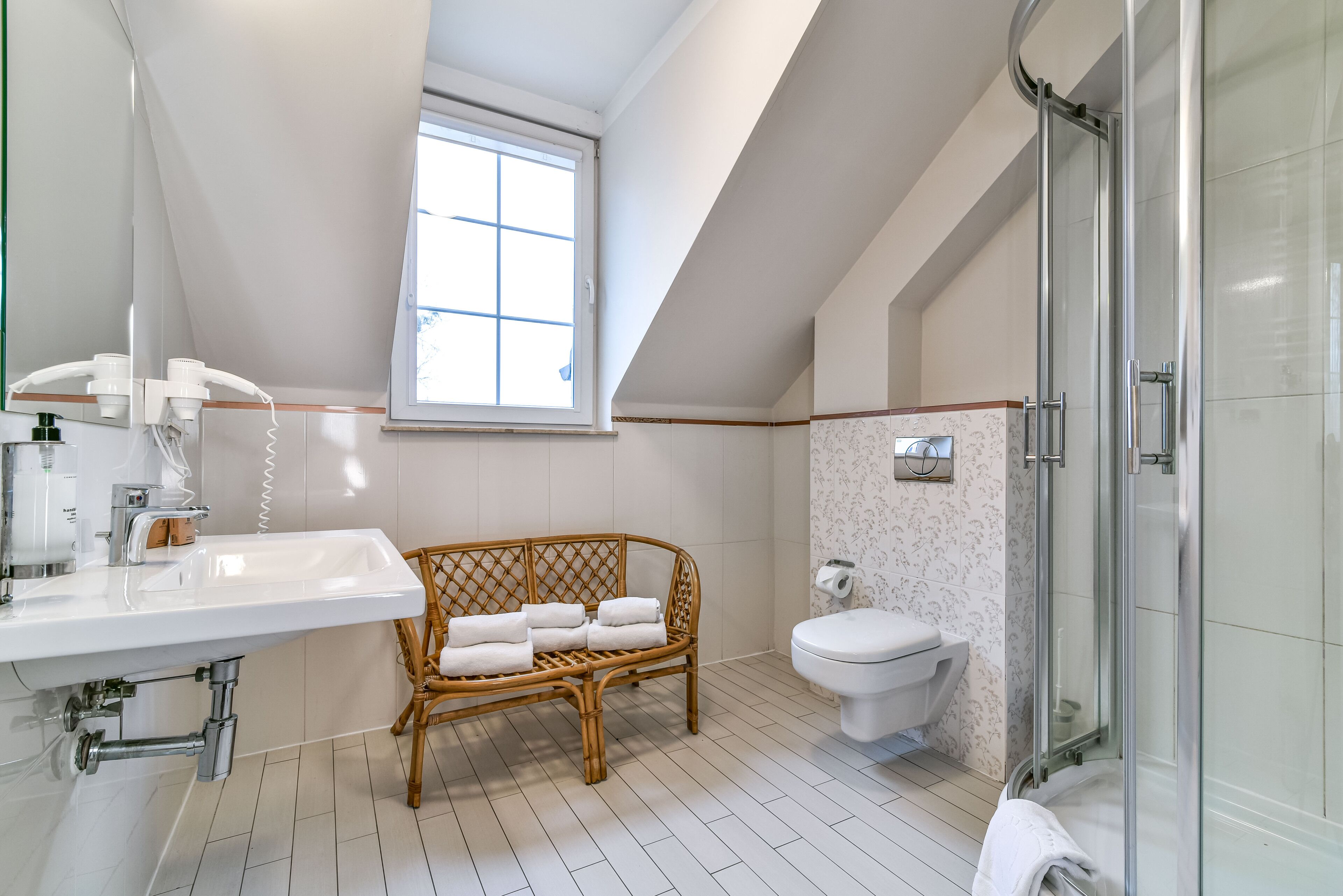 A modern bathroom with a white sink, a glass shower enclosure, a toilet, and a window providing natural light.