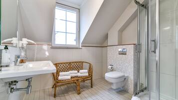 A modern bathroom with a white sink, a glass shower enclosure, a toilet, and a window providing natural light.