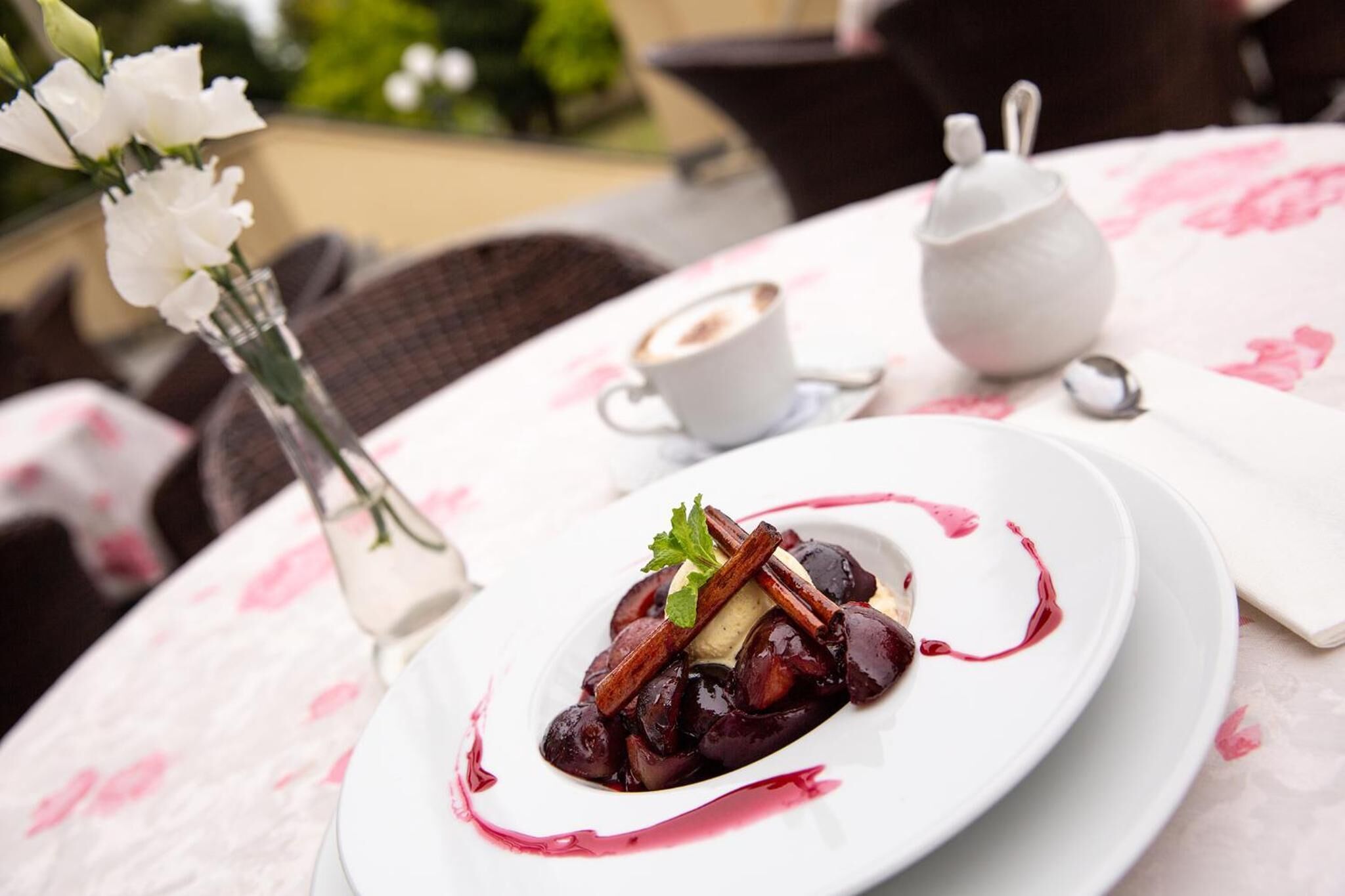 A dessert plate with a white tablecloth, a small white teapot, and a cup of coffee on a table.