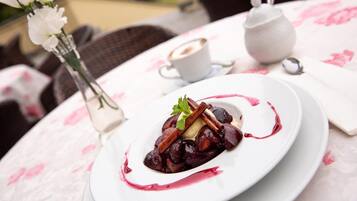 A dessert plate with a white tablecloth, a small white teapot, and a cup of coffee on a table.