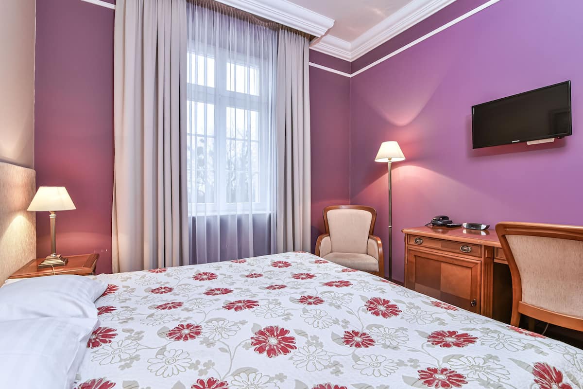 Une chambre d’hôtel équipée d’un lit, d’un bureau, d’une chaise, d’une télévision et d’une fenêtre avec des rideaux.