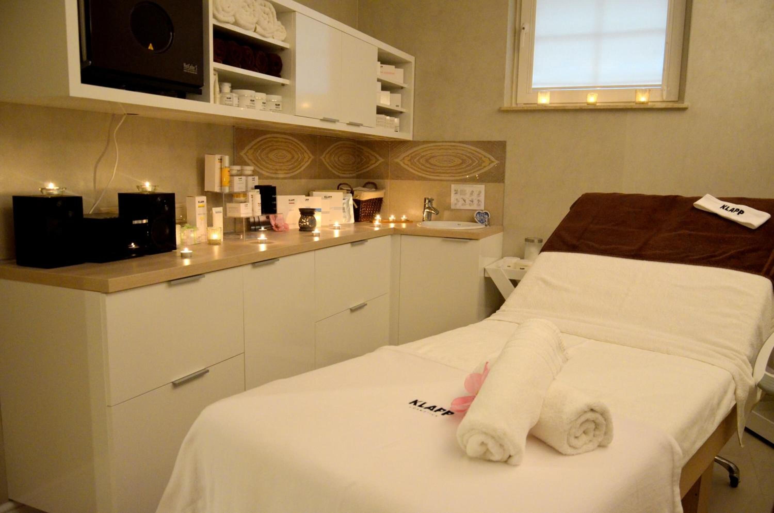 A hotel room with a bed, a bedside table, a small desk, a shelf with toiletries, and a window with a view.