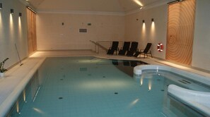An indoor swimming pool with a few lounge chairs and a hot tub.