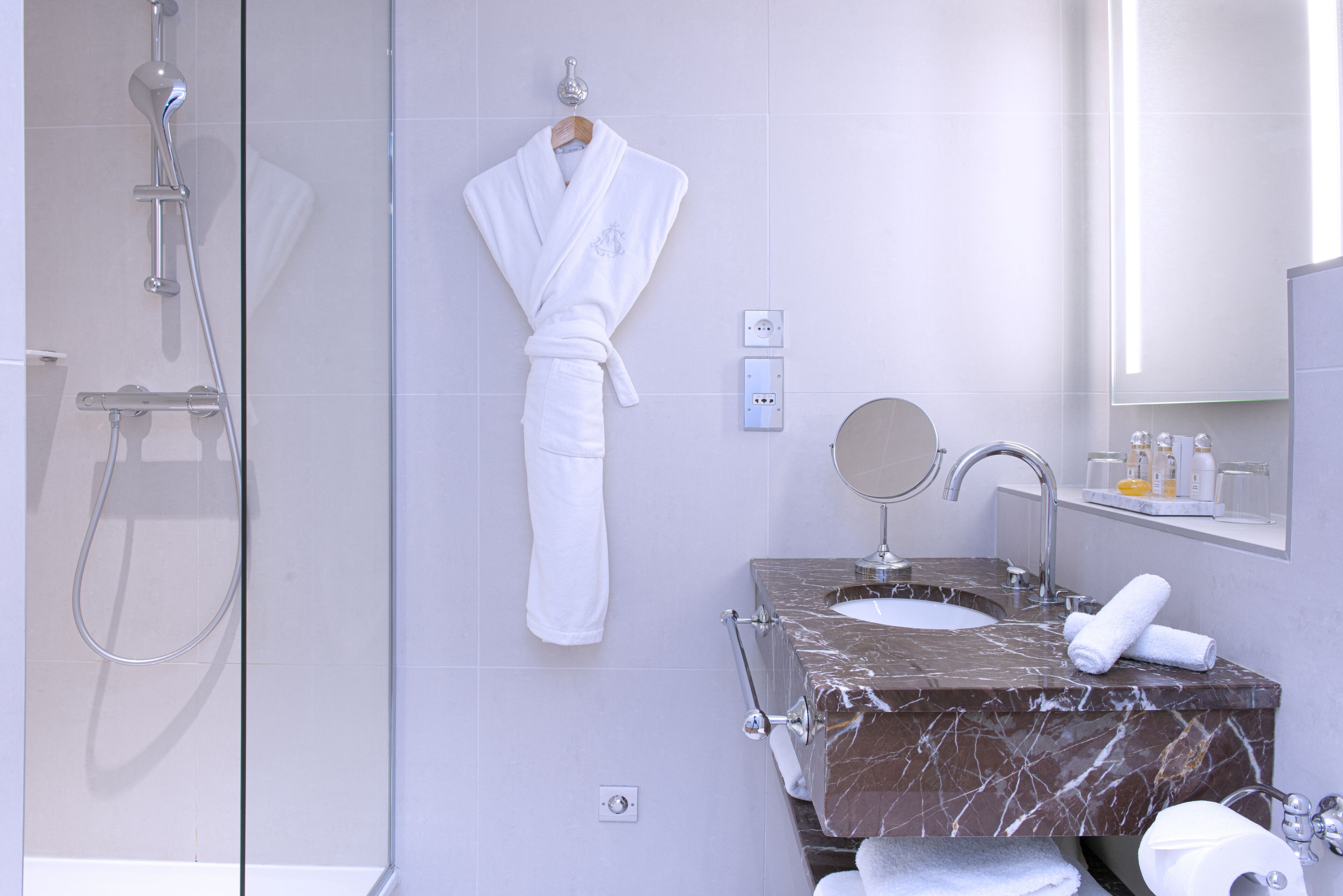 A modern bathroom with a glass-enclosed shower, a marble sink, and a hanging robe.