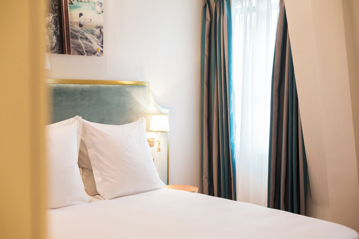 Una habitación de hotel con una cama bien hecha, una lámpara en la mesita de noche y cortinas en la ventana.