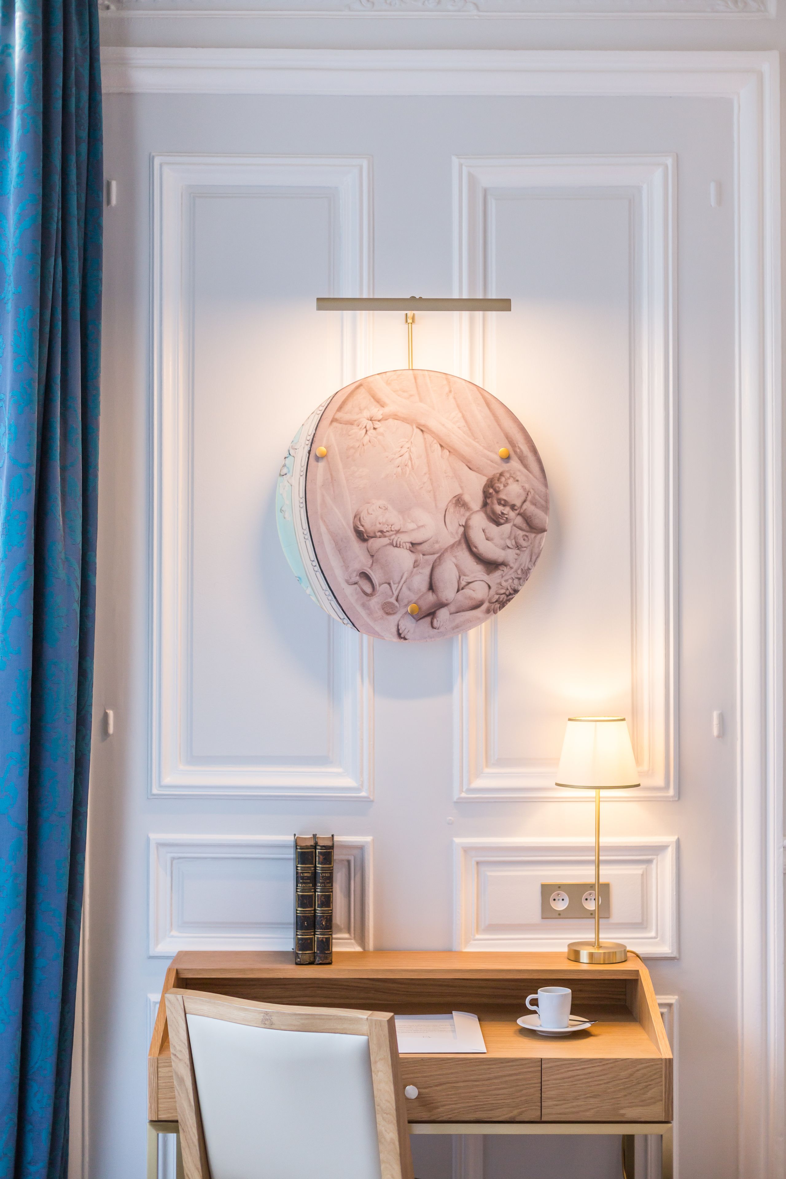 A room with a wooden desk, a white chair, a lamp, a wall-mounted globe, and a blue curtain.