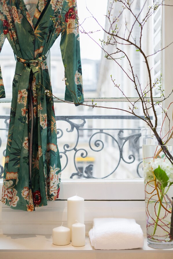 A window with a floral robe, candles, and a vase with a branch.