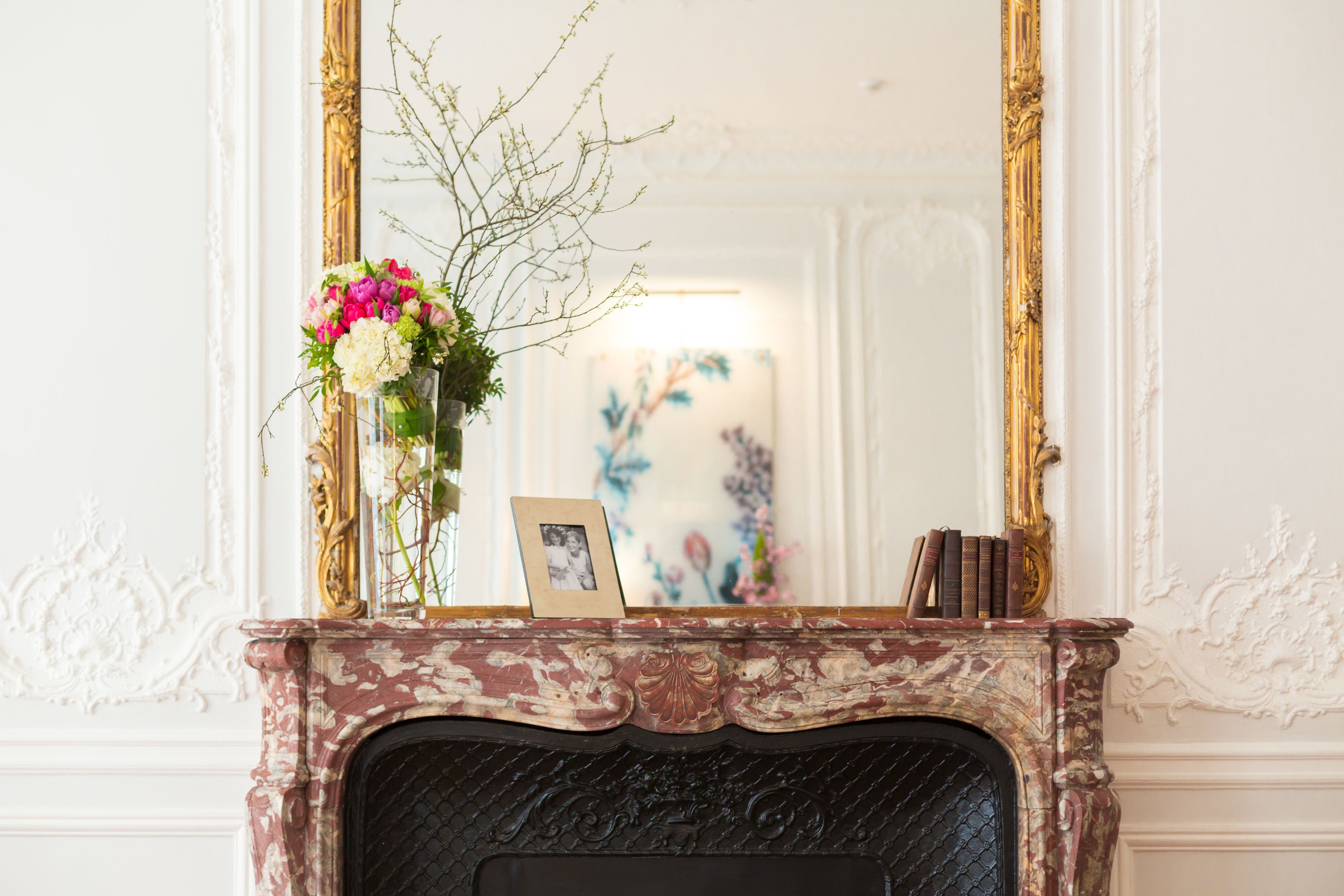 A fireplace with a mirror above it, a vase with flowers, and a framed photo on the mantel.