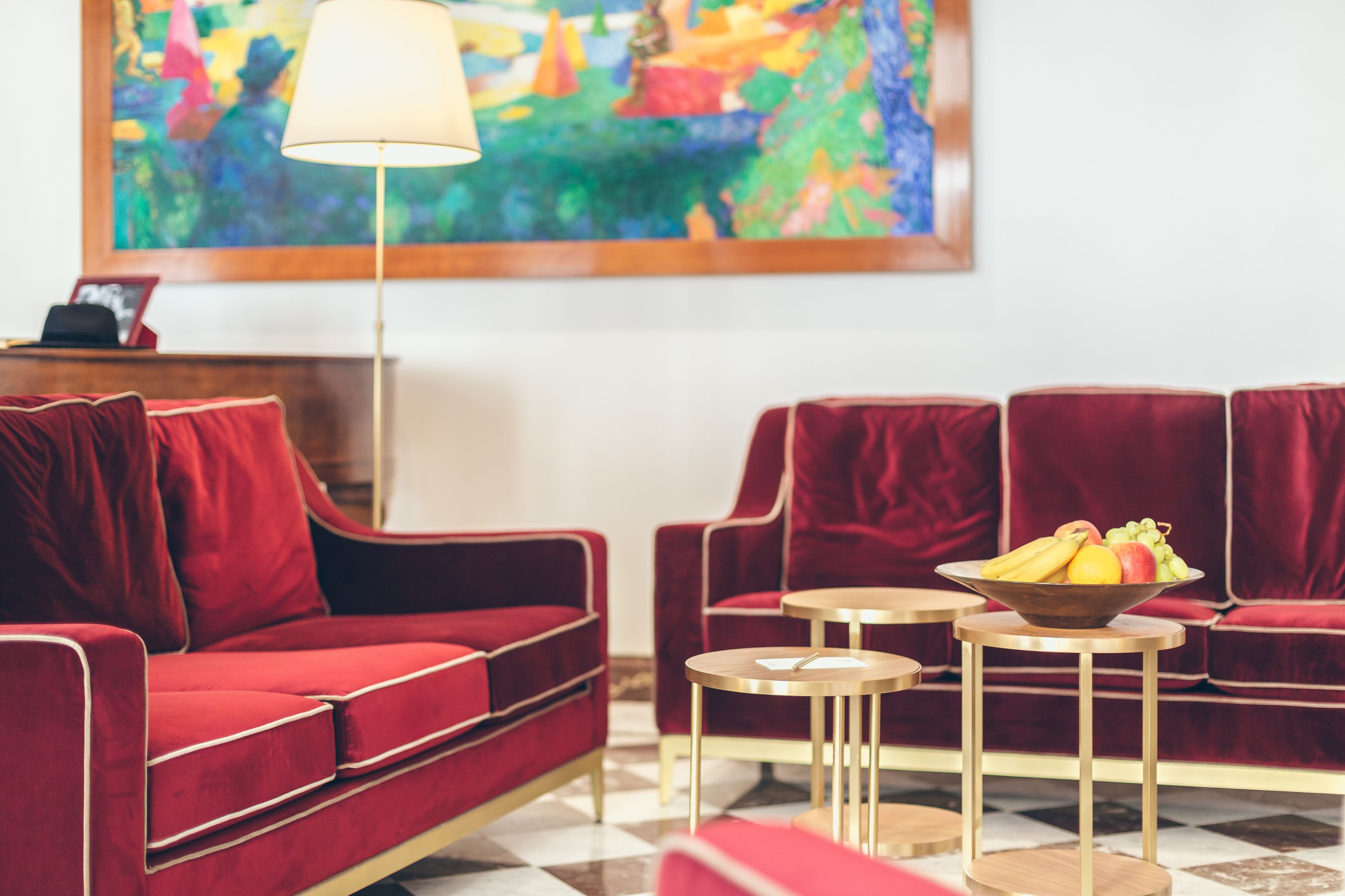 A red sofa set with a bowl of fruit on a small table, a lamp, and a colorful painting on the wall.