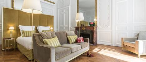 A hotel room with a bed, a sofa, a chair, a mirror, and a fireplace.