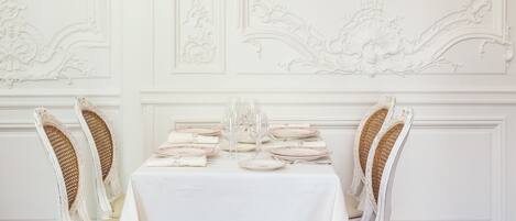 A dining room with a white table set for four, white upholstered chairs, and a framed portrait on the wall.