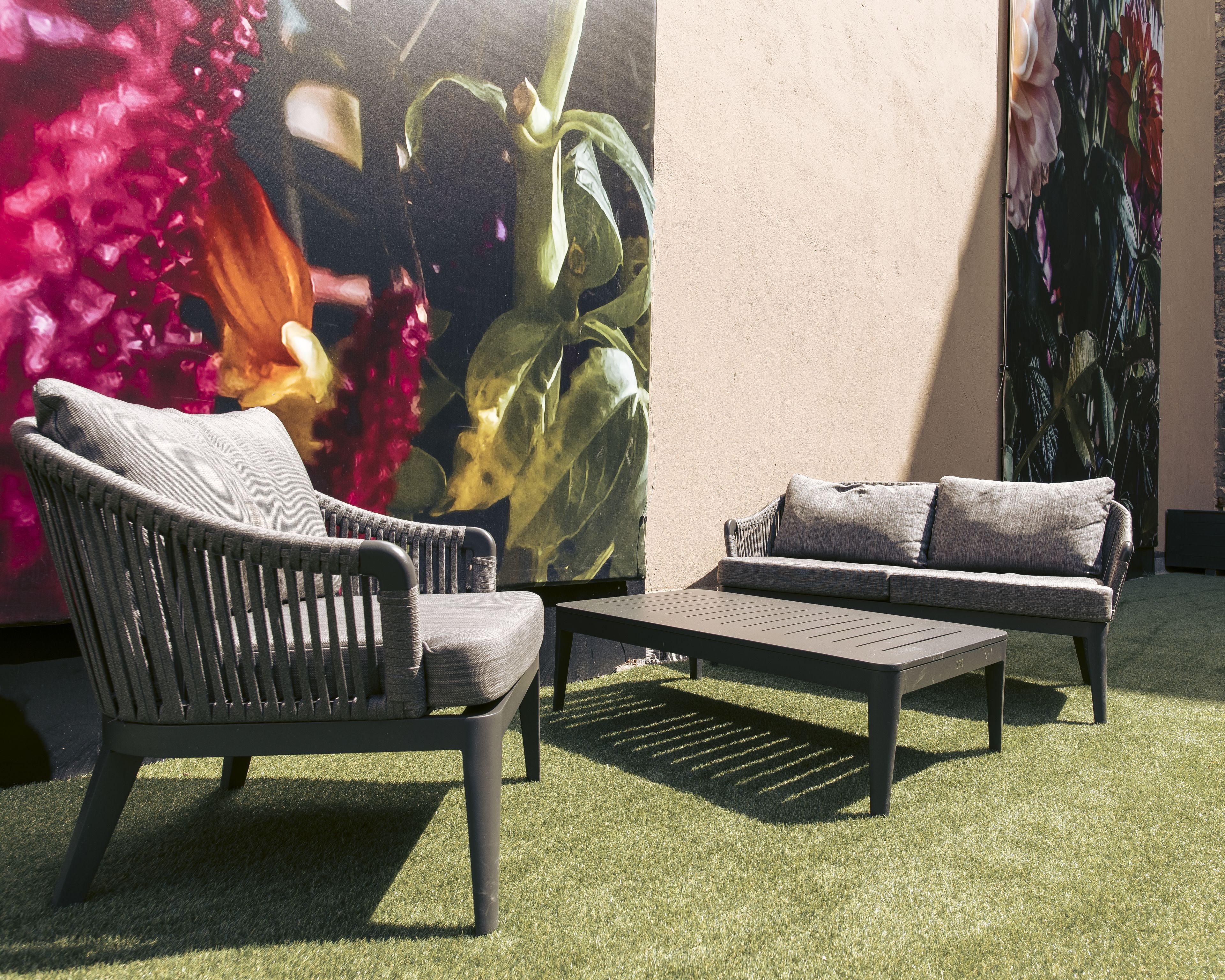 A seating area with two sofas and a coffee table, set on artificial grass, against a wall with a large floral mural.