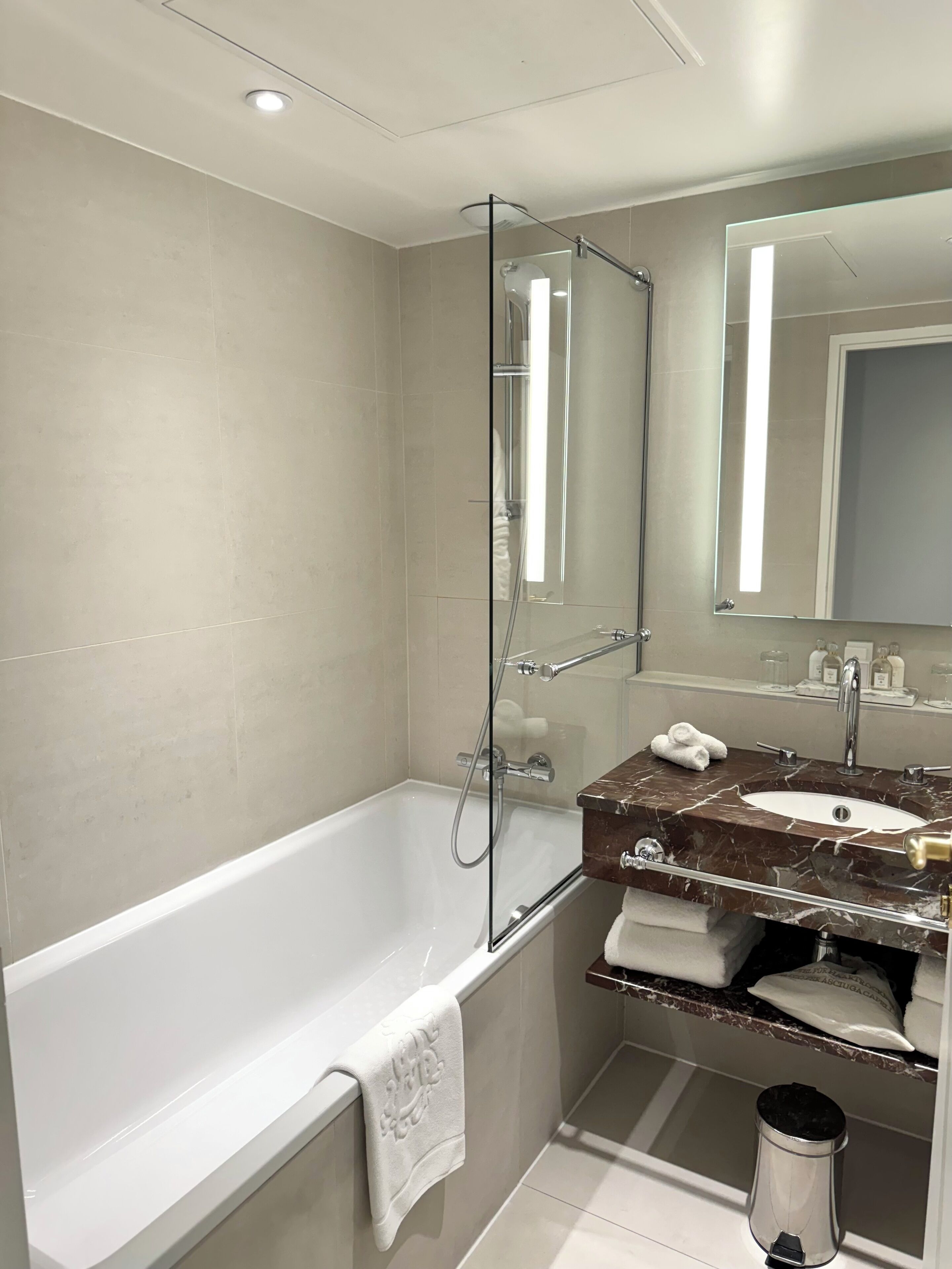 A modern bathroom with a bathtub, a glass-enclosed shower, a marble sink, and a large mirror.