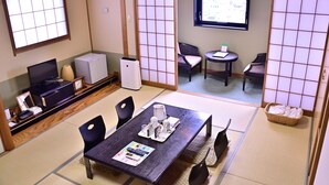 A traditional Japanese room with tatami flooring, a tatami mat table, black chairs, a television, a refrigerator, and a sliding door leading to another room. - Takasaki Urban Hotel (Takasaki)