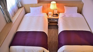 A hotel room with two beds, each with white and purple bedding, a bedside table with a lamp, and a small nightstand with a phone and a notepad. - Takasaki Urban Hotel (Takasaki)