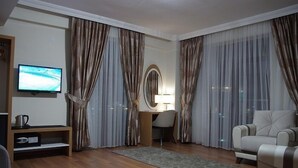 A modern living room with a flat-screen TV, a desk with a lamp, and two armchairs. - Gevher Hotel (Kayseri)