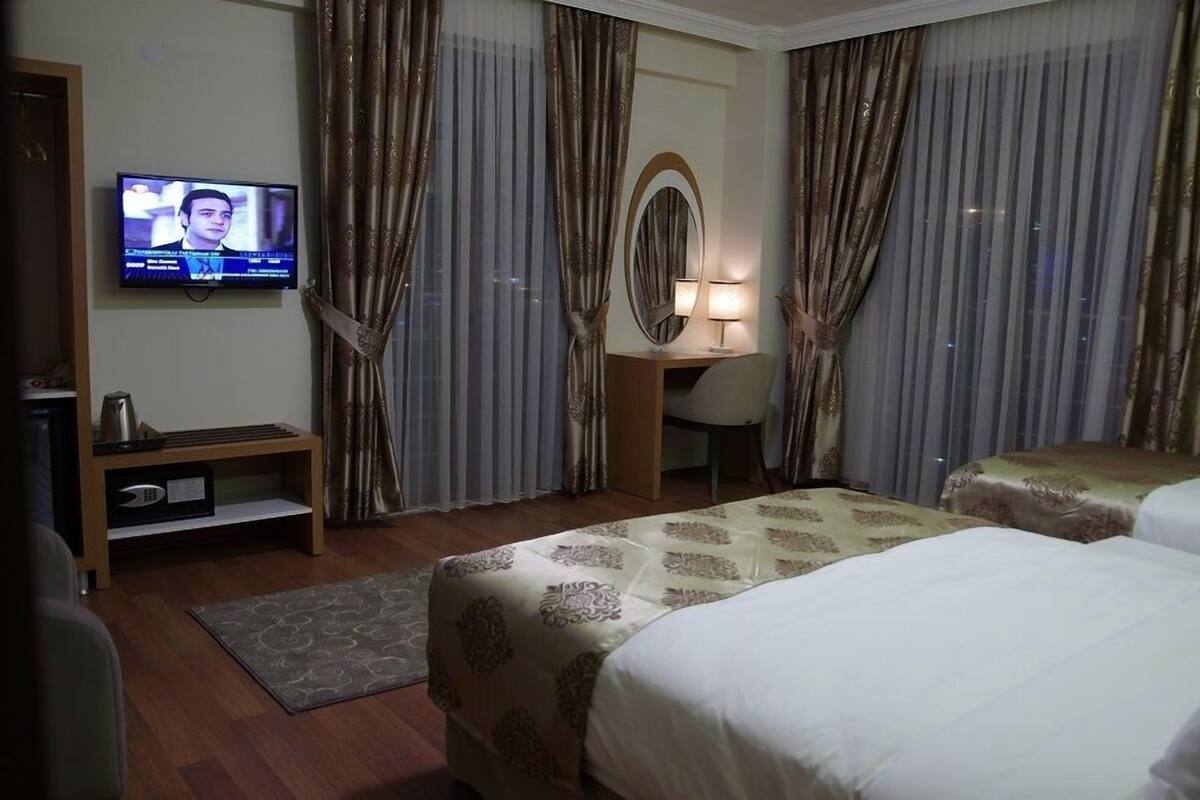 A hotel room with two beds, a television on the wall, a desk with a lamp, and curtains.