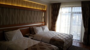 A hotel room with two beds, a wooden headboard, a nightstand, and a large window with curtains. - Gevher Hotel (Kayseri)