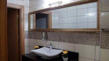 A bathroom with a white sink, a mirror with a gold frame, and a tiled wall.