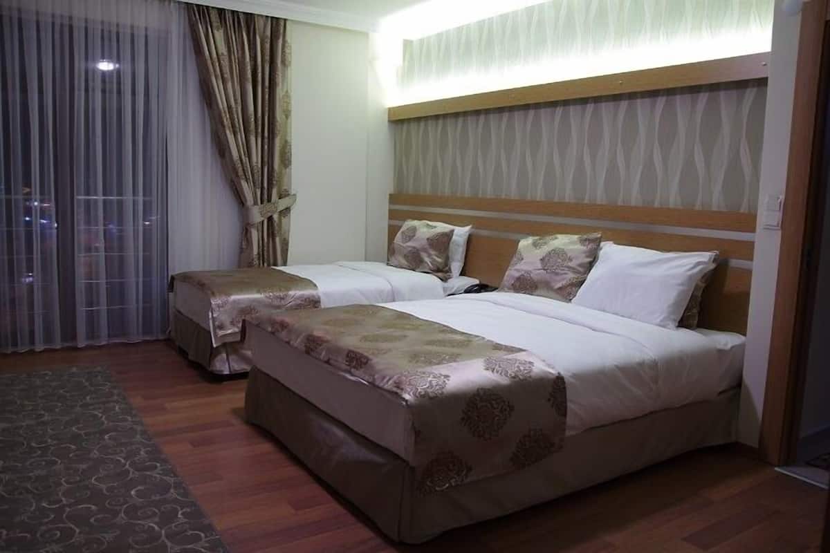 A hotel room with two beds, a wooden headboard, a large window with curtains, and a patterned rug.