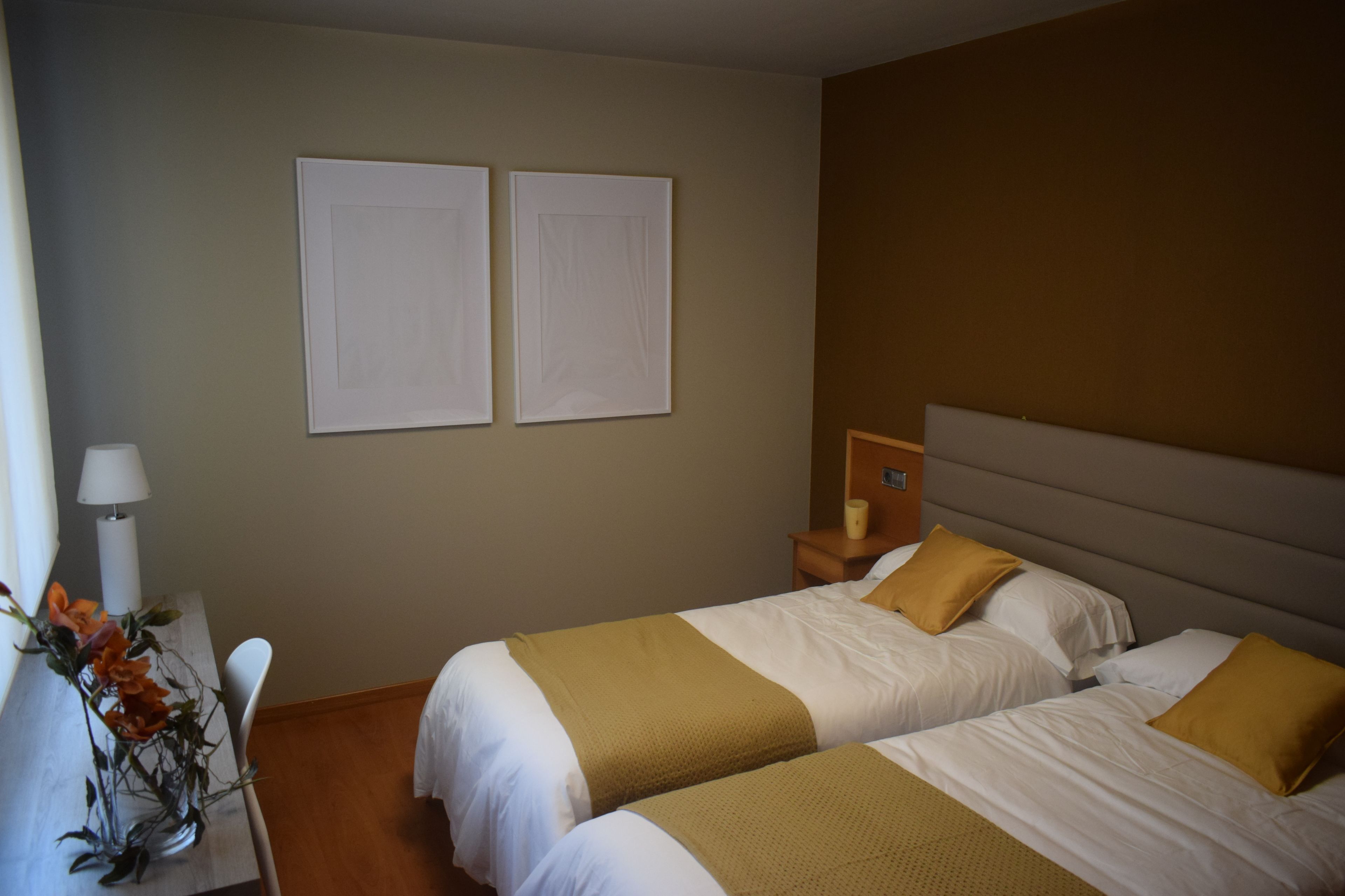 Habitación de hotel con dos camas, una mesita de noche, una lámpara y un florero con flores.
