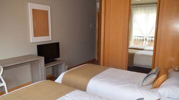 Habitación de hotel con dos camas, un escritorio con televisor y un balcón con vistas.