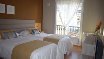 Habitación de hotel con dos camas, un televisor, un balcón y vistas a edificios.