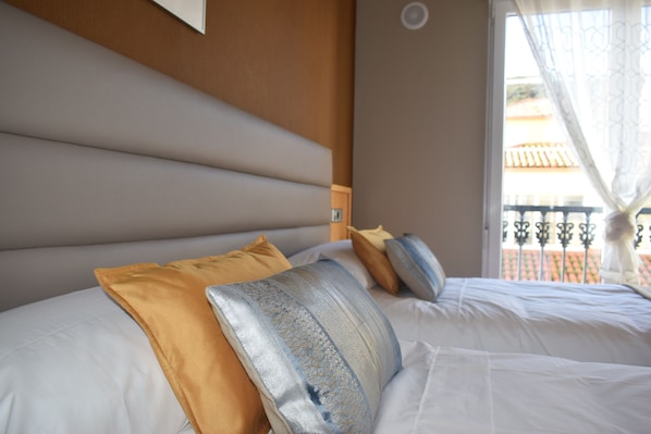 Una cama bien hecha con cabecera, varios almohadones y vistas a un balcón con barandilla.