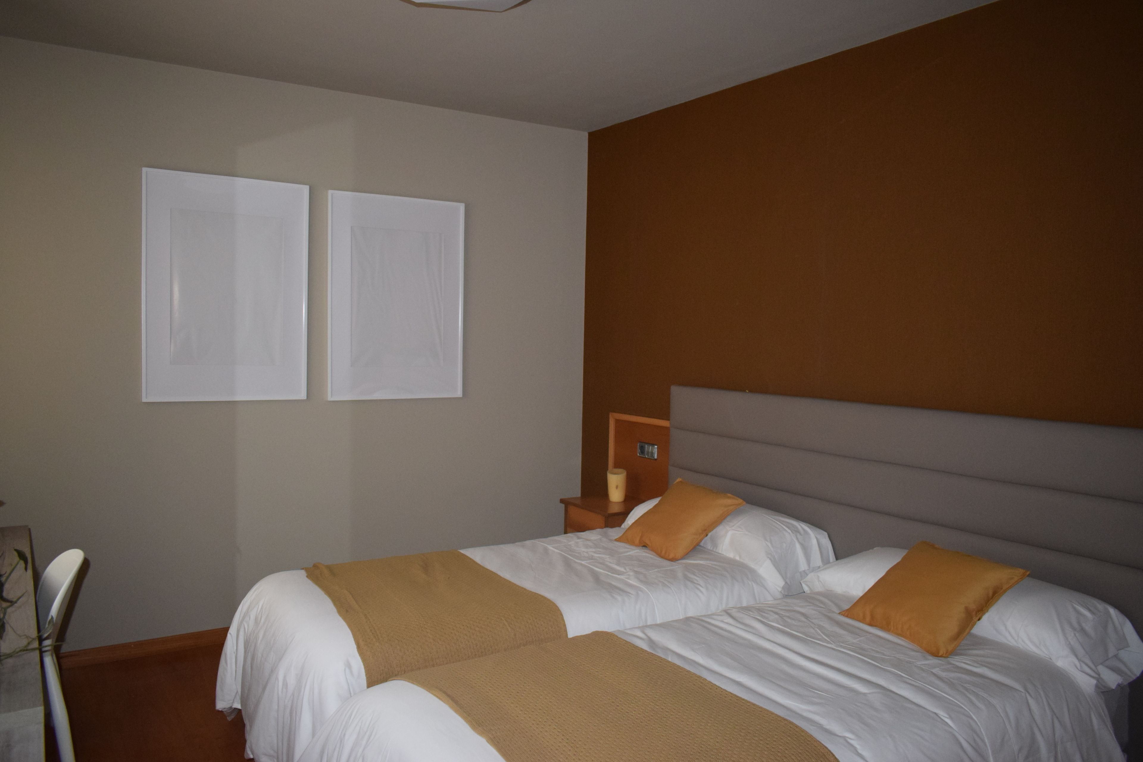 Habitación de hotel con dos camas, una mesita de noche y un reloj en la pared.
