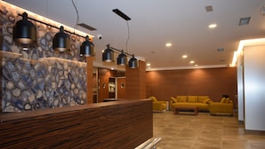 Un área de recepción con un mostrador de madera, una pared de piedra y una sala de estar con sofás amarillos.