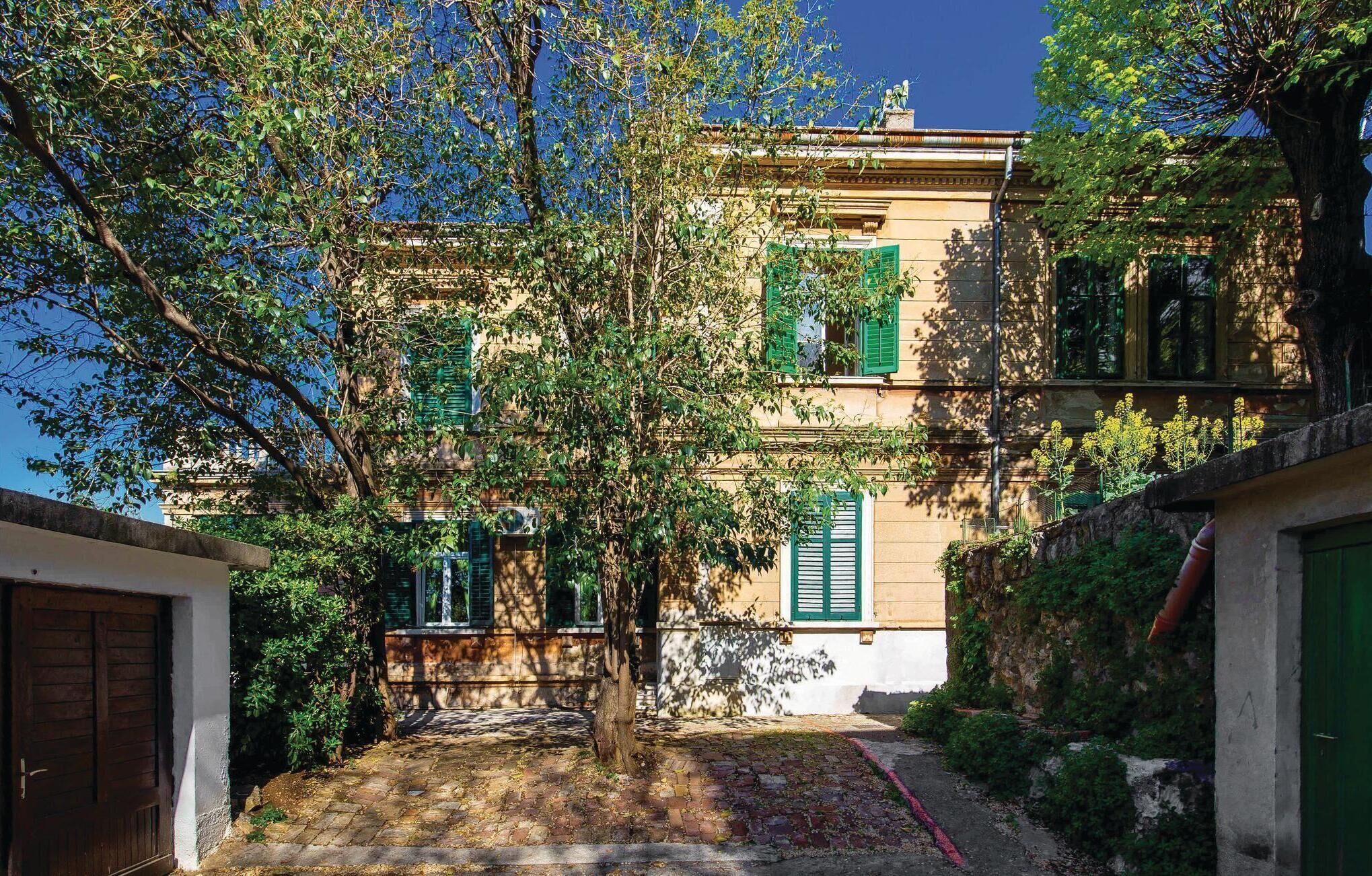 A courtyard with a building featuring green shutters and a stone pathway.