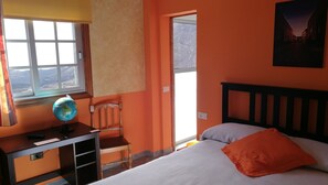 Une chambre à coucher avec un lit, un bureau sur lequel se trouve un globe terrestre, une chaise et une fenêtre donnant sur un beau paysage.