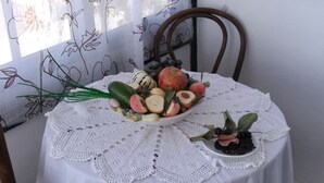 A round table with a white tablecloth and lace doily, set with a bowl of fruit and a potted plant.
