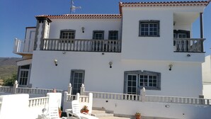 A two-story building with balconies, a white facade, and a tiled roof.