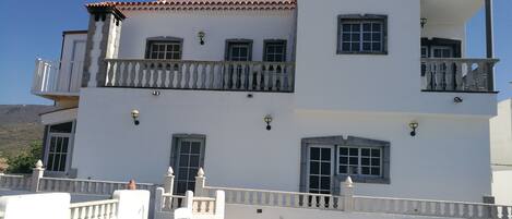A two-story building with balconies, a white facade, and a tiled roof.