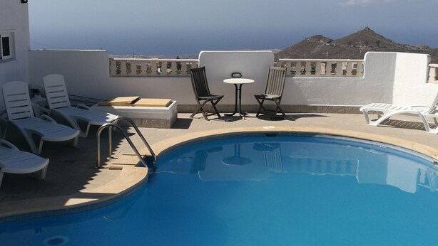 A rooftop pool with lounge chairs and a table, overlooking a mountainous landscape.