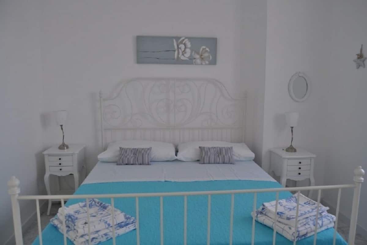 Une chambre à coucher bien rangée, avec un lit blanc, deux tables de chevet, un élément décoratif mural et un ornement en forme d’étoile.