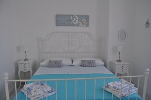 Un dormitorio ordenado con una cama blanca, dos mesitas de noche, un adorno de pared decorativo y un adorno con forma de estrella.