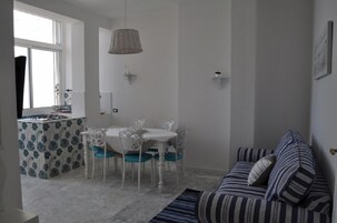 Un área de comedor con una mesa y sillas blancas, una lámpara colgante y un sofá a rayas en primer plano.